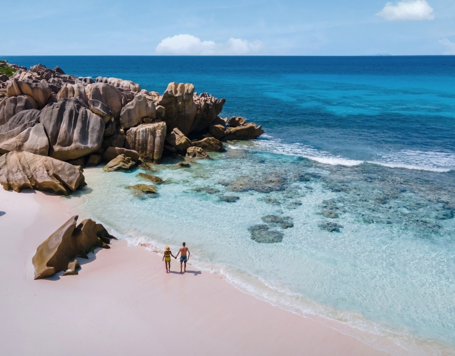 This serene beach scene, part of an MSC cruise vacation experience, features a couple holding hands as they leisurely stroll along the rocky shoreline under a soft-clouded sky. It encapsulates the natural coastal beauty, tranquility, and relaxation you can enjoy while on your MSC cruise getaway. 