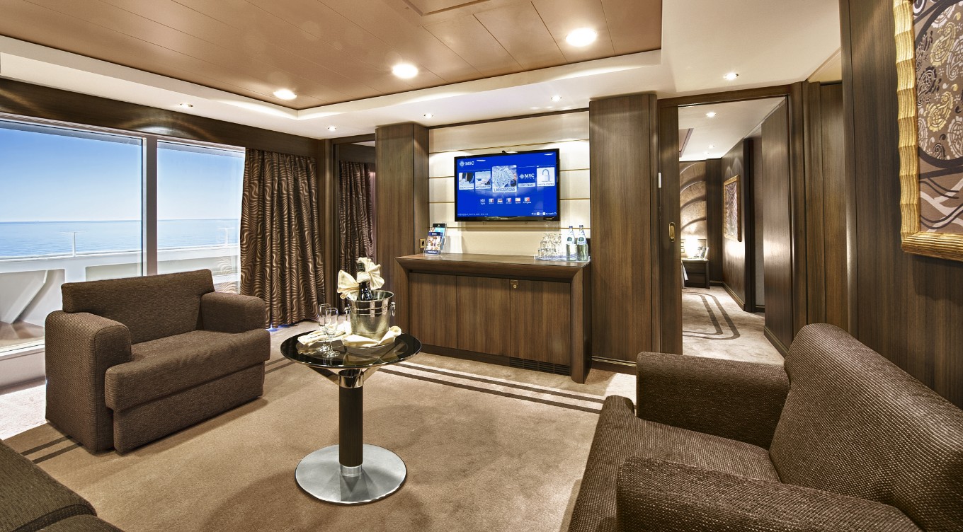 This inviting indoor living room is part of the Executive Family Suite on MSC Divina. It features a warm brown color theme with two comfortable couches surrounding a central coffee table with a television for everyone to enjoy on your family cruise vacation.