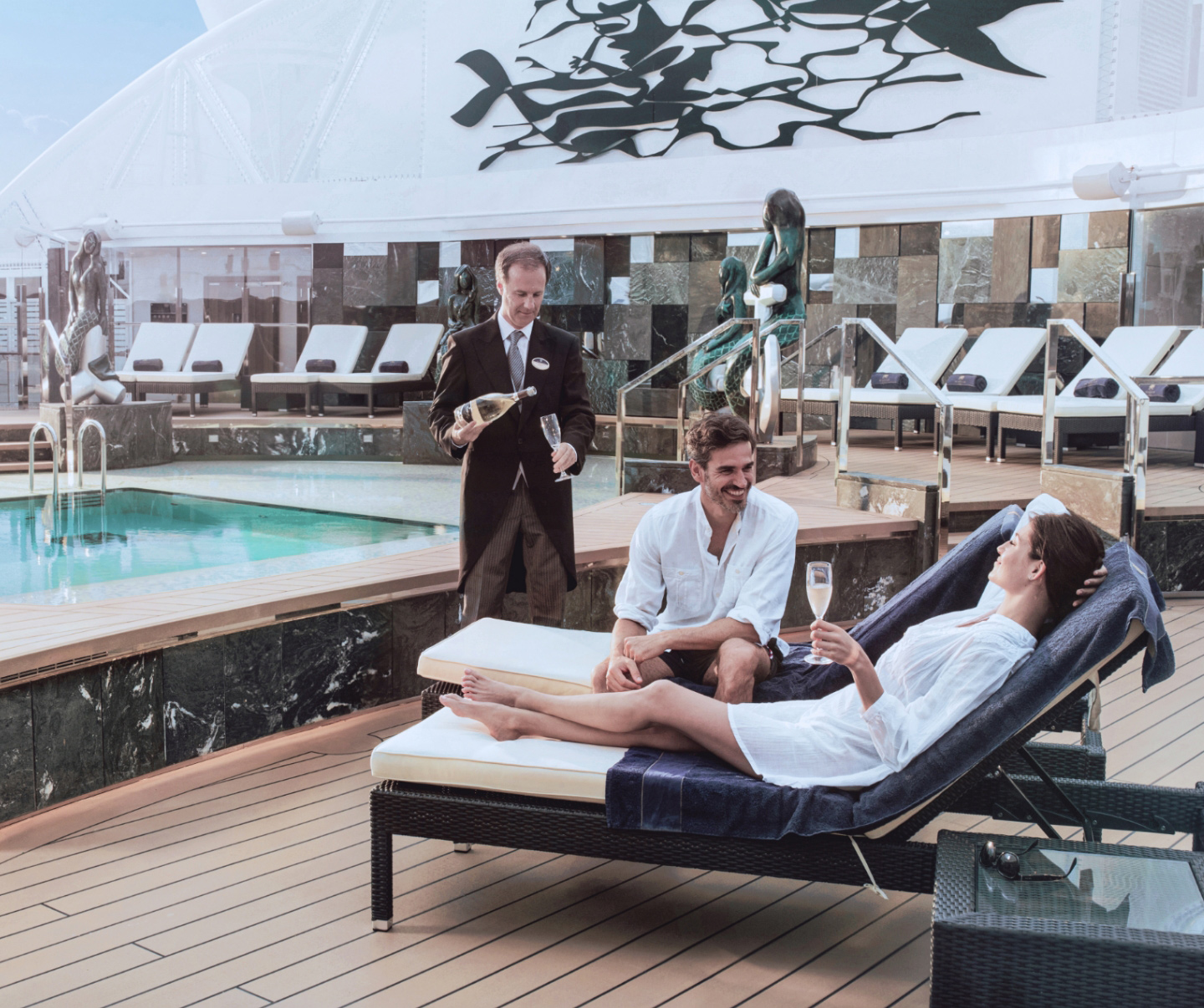 Indulge in the Yacht Club's exclusive Private Solarium on MSC Cruises, where a couple is pampered by a butler, offering personalized service for drinks, food, towels, and more. The image features a crystal-clear, elevated hot tub, epitomizing luxury and relaxation. 