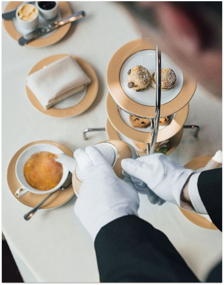 A MSC Yacht Club butler in white gloves serves cruises guests tea and coffee with delicious pastries on a tiered.